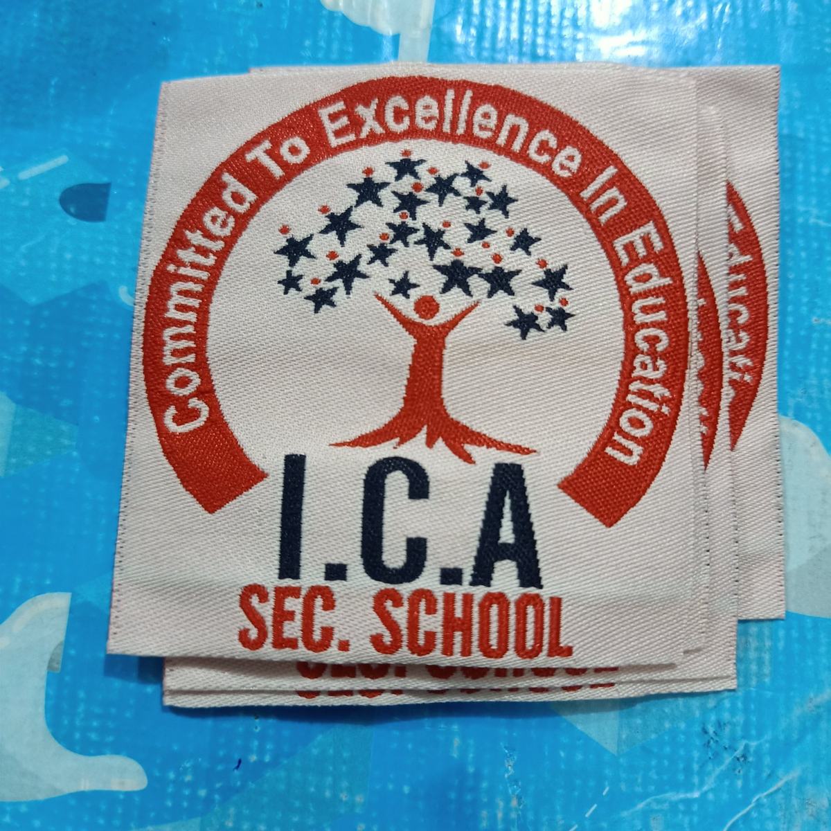 Woven school badge for I.C.A Sec. School, red and navy crest on cream