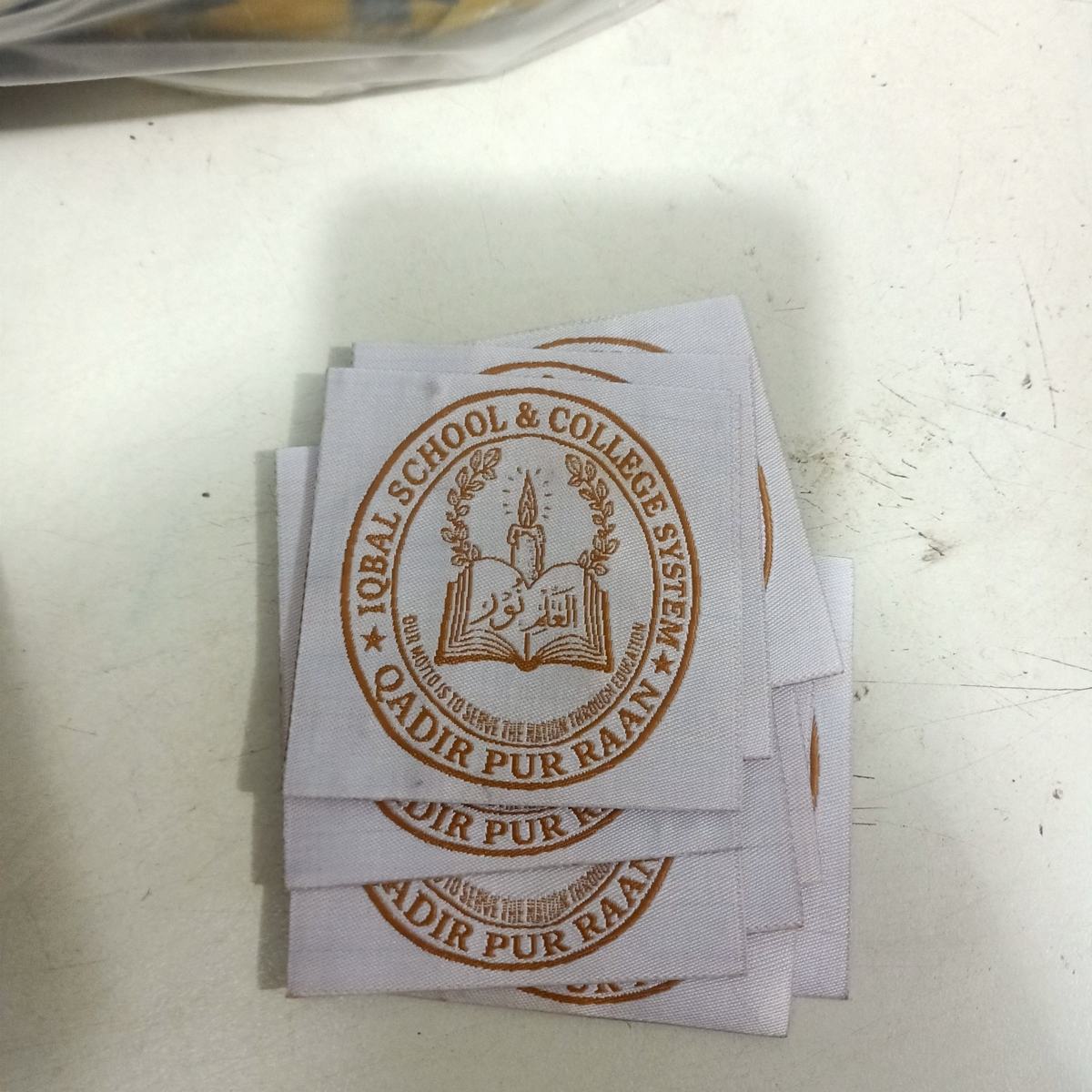 Circular woven school badge for Iqbal School and College System, gold on white